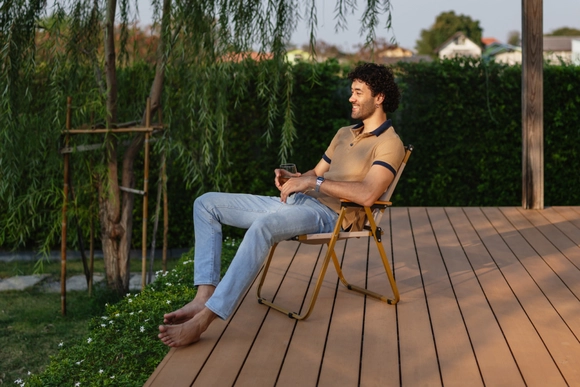 Ein Mensch entspannt barfuß auf einem Klappstuhl auf einer Holzterrasse.